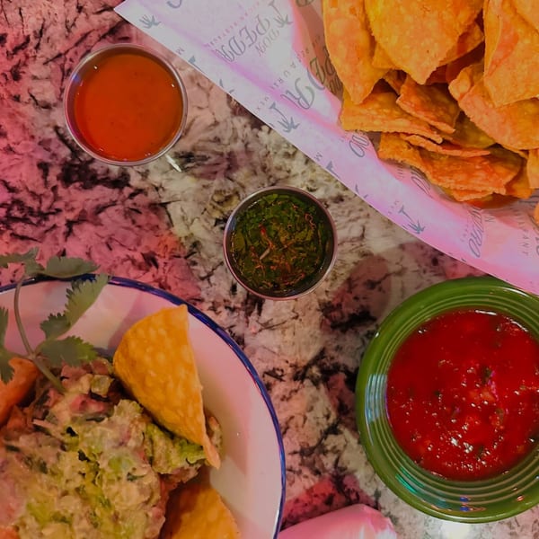 Overhead view of Don Pedro Mexican Restaurant's chips, salsa, guacamole, and green sauce on a marble table.